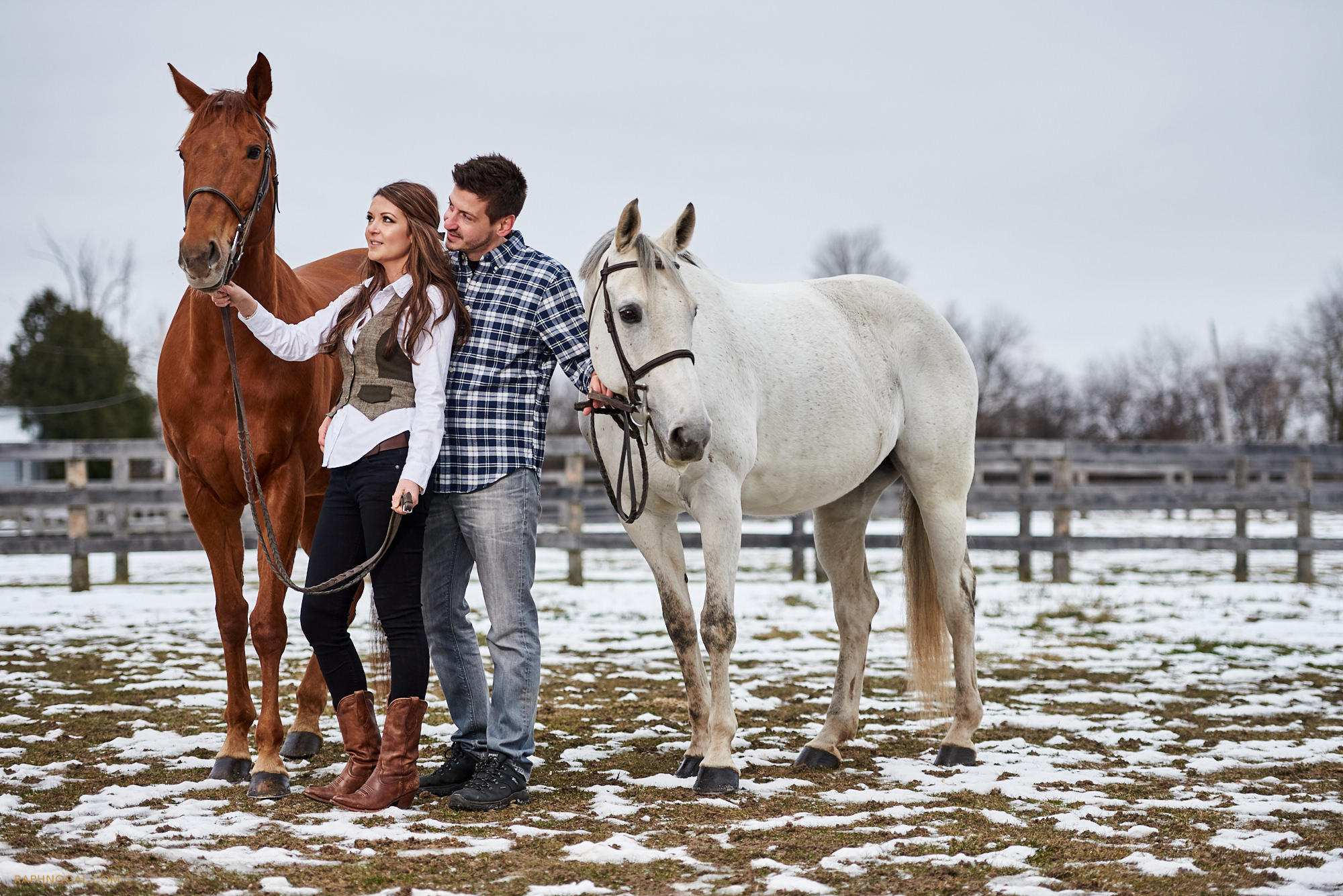 Couple standing with horses at Stonewood Equestrian during engagement shoot