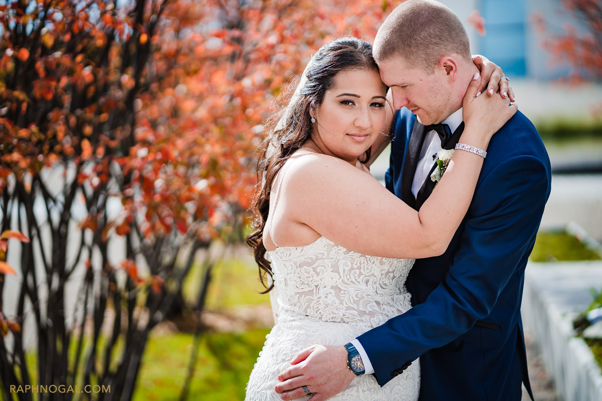 Bride and Groom hug by red trees at Aga Khan