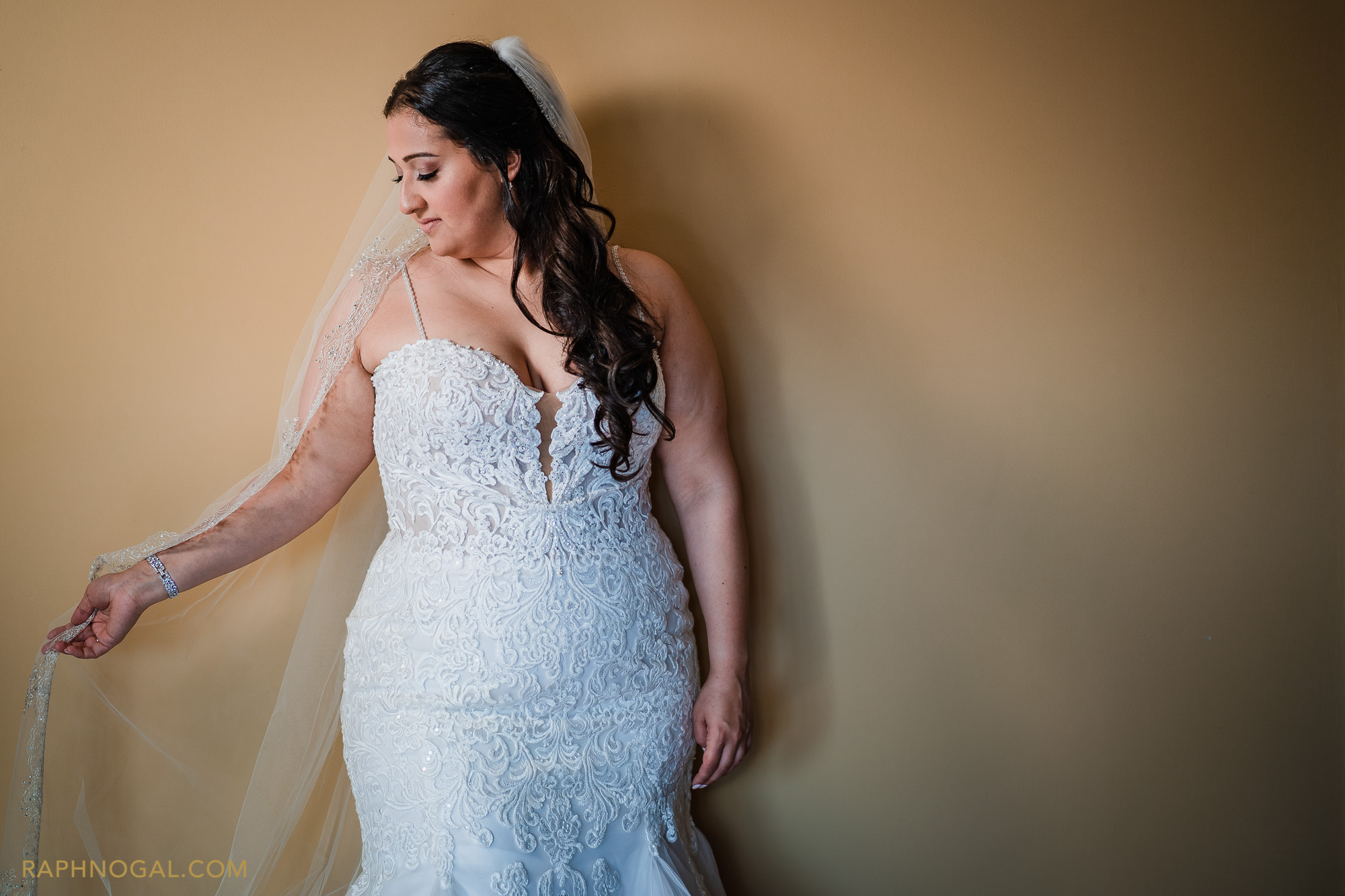 Bride playing with veil against yellow wall